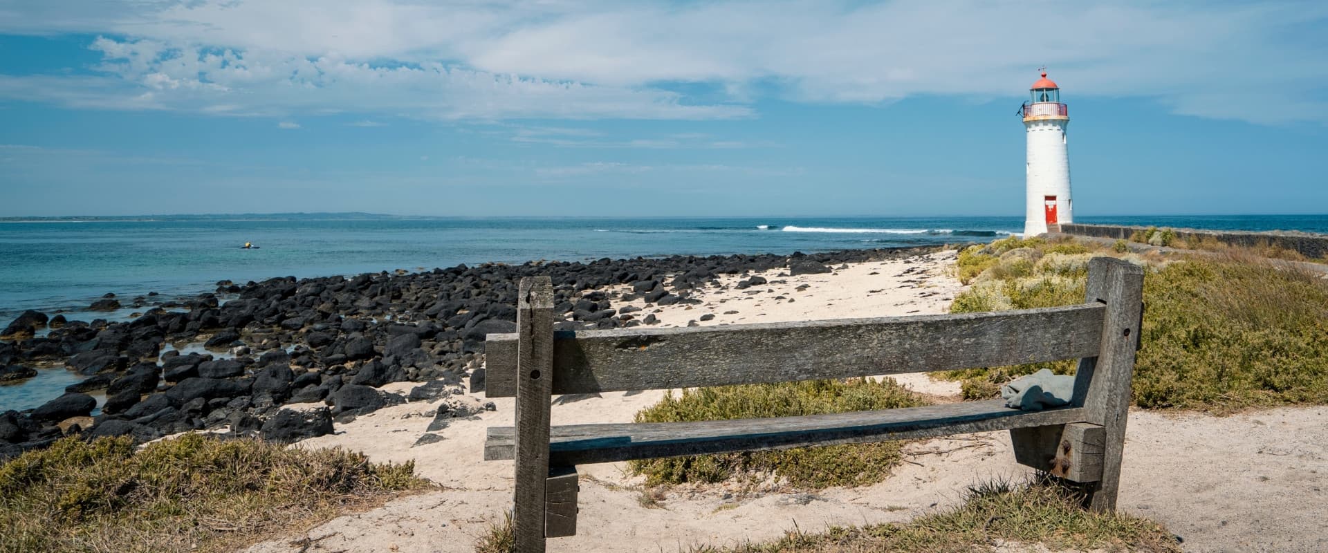 Bench on the beach overlooking a lighthouse.