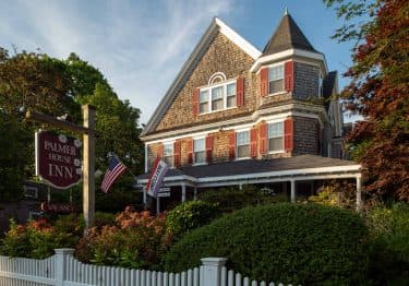 Palmer House exterior at sunset with brown siding and red shutters and a fenced-in garden