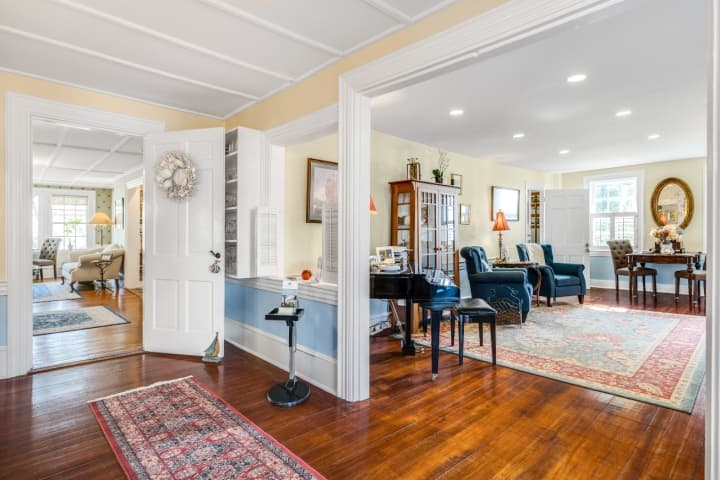 Elegant parlor and guest entrance with polished wood floors, vintage rugs, and a grand piano, offering a welcoming common area at the inn.