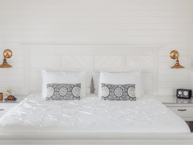 Bright and airy guest room with white linens, matching shiplap walls, brass sconces, and charming breakfast setup.