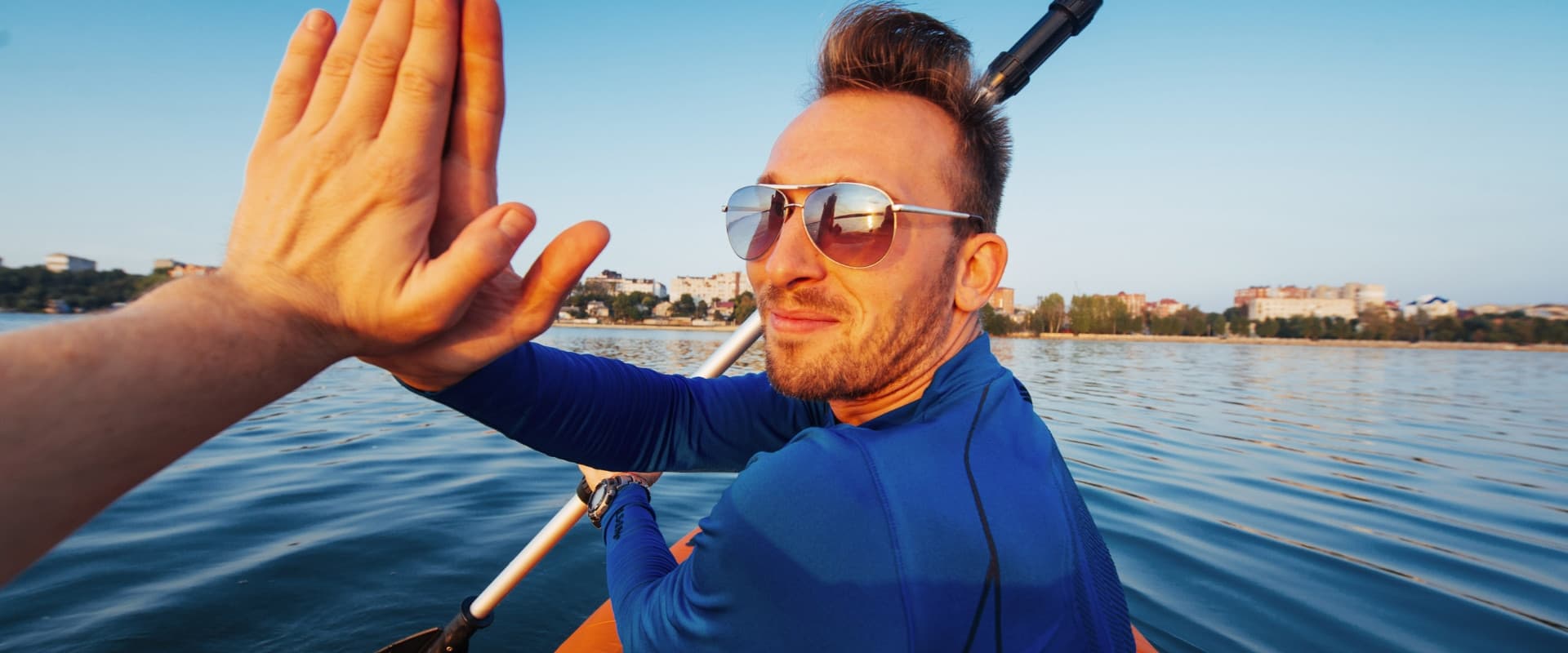 Two friends high-five on a lake in a kayak
