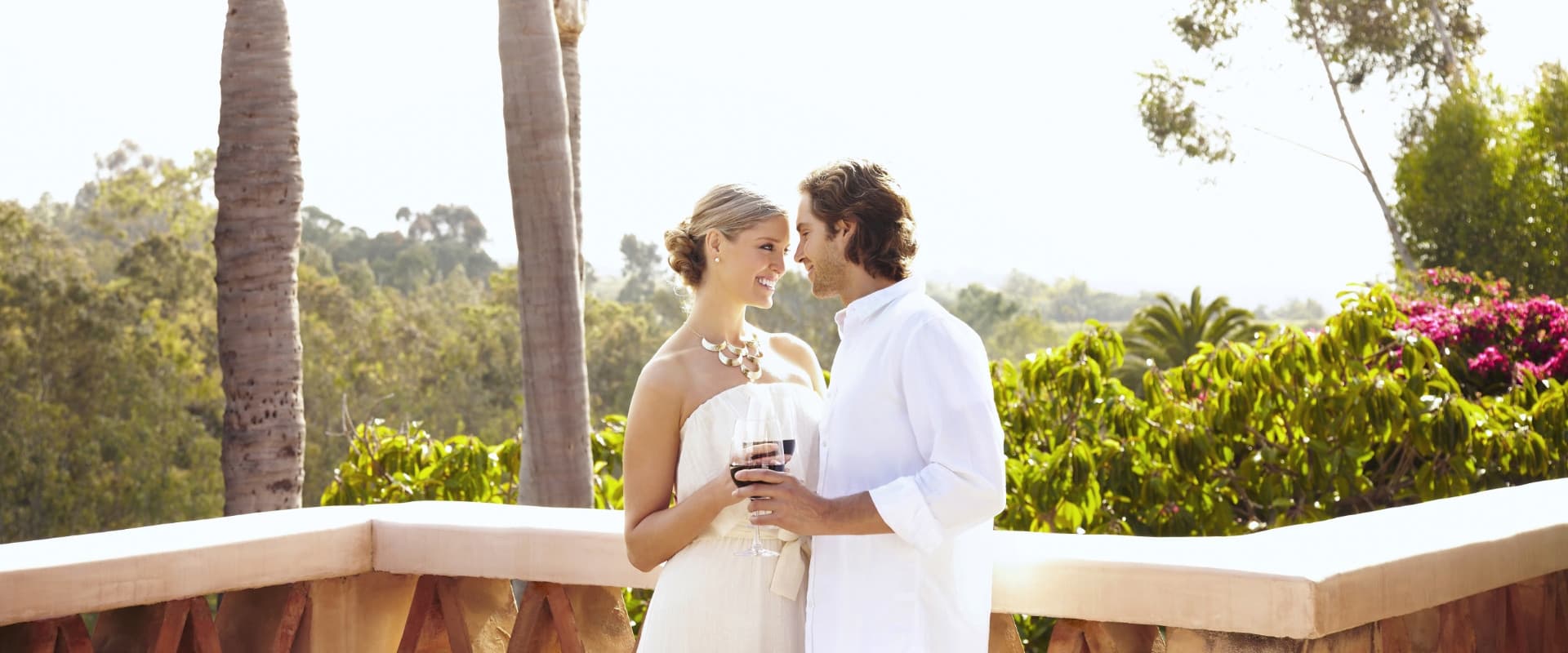 Glamorous couple drinking red wine on a veranda.