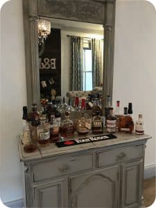 A bar cart with various bottles of liquor and a mirror