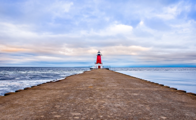 A long pathway surrounded by the ocean with a lighthouse at the end.