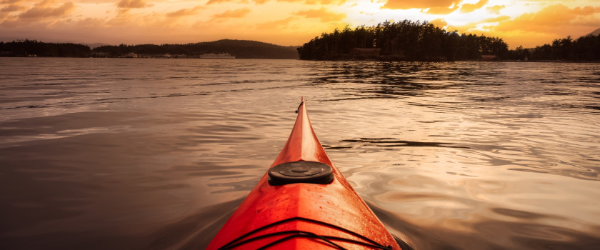 A sea kayak paddling in the Pacific Ocean at sunset.