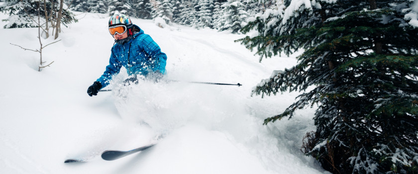 A girl skiing between trees in deep snow.