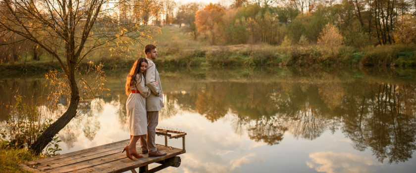 A romantic young couple stands on a pier near a lake