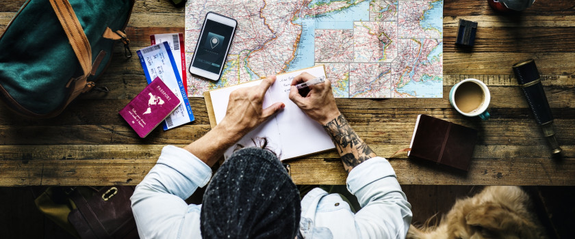 Aerial view of a person planning a trip on a desk with a map and notebook.