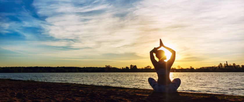 A person does yoga exercises on a lake at sunrise