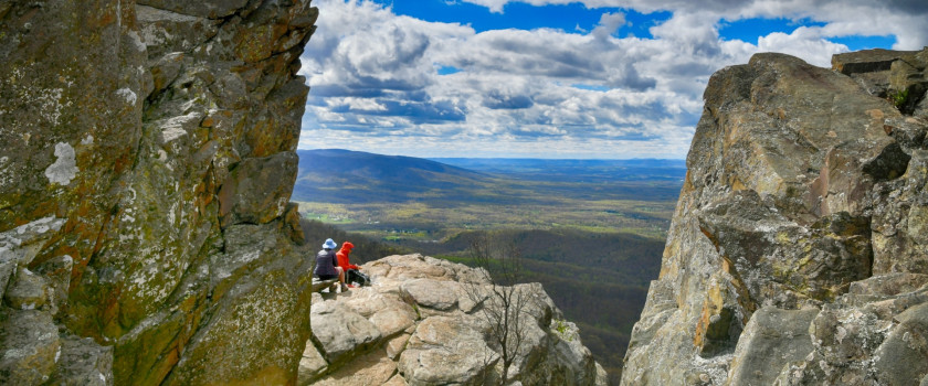 A couple having a picnic on a rock ledge overlooking rolling hills.