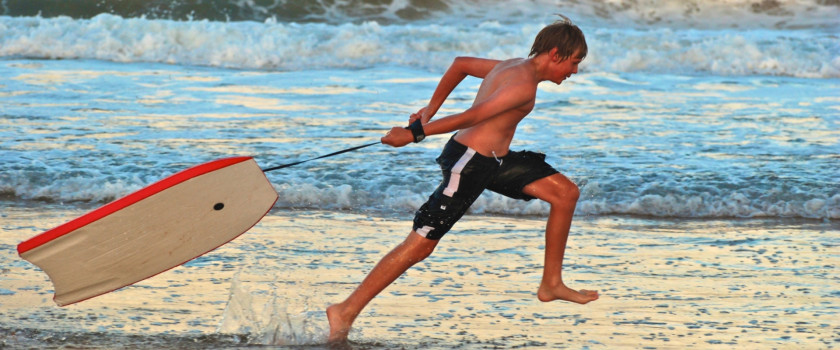 Young boy running with a boogie board on the beach