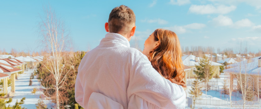 Honeymooning couple in robes overlooking trees in the winter