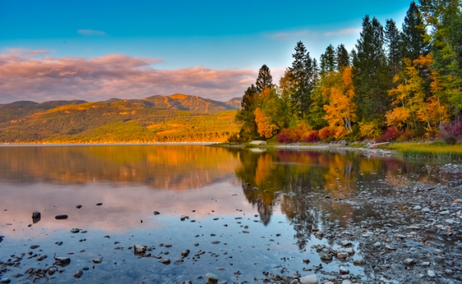 A lake surrounded by trees and rolling hills in the distance during the fall.