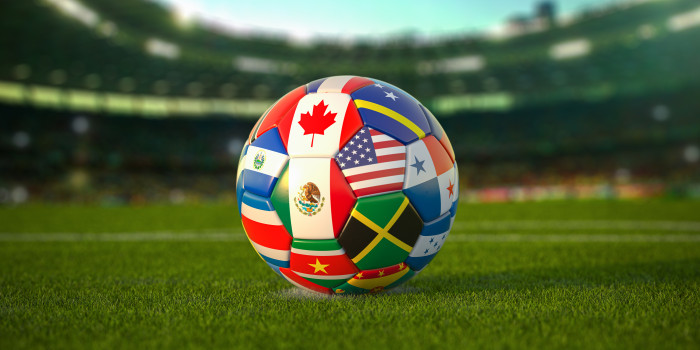 Soccer ball with the flags of many nations on a green soccer field with stadium in the background