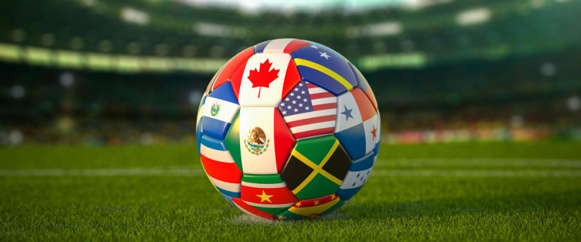 Soccer ball with the flags of many nations on a green soccer field with stadium in the background