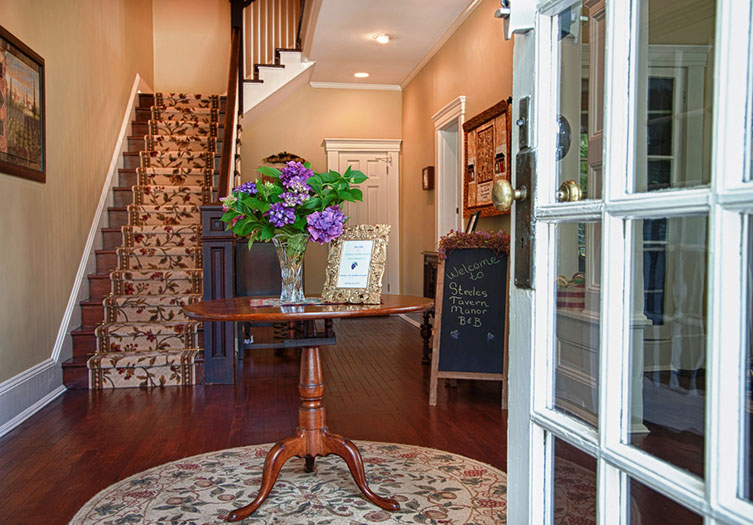 Beautifully decorated foyer entry of the B&B with hardwood floors, center round table, and staircase to the upstairs