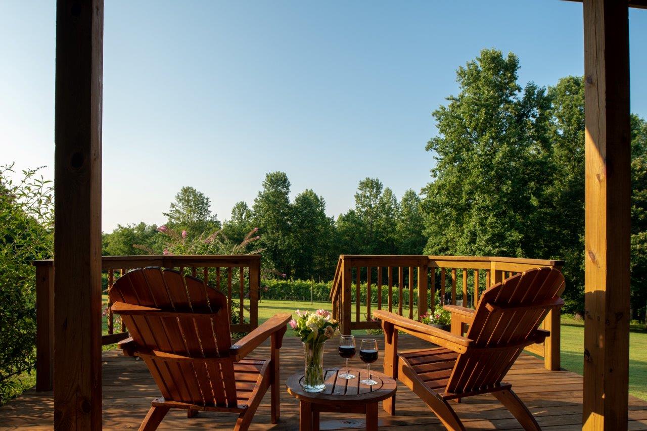 Arcady's Madison Suite deck with wood Adirondack chairs and a table overlooking lush green grass and trees