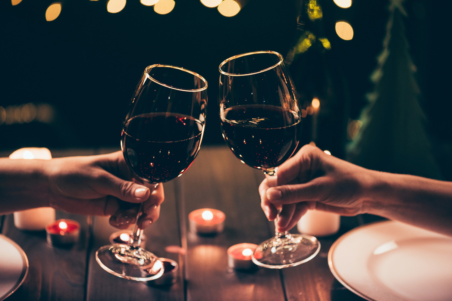 Cropped shot of two women clinking glasses with wine over served table with lit candles