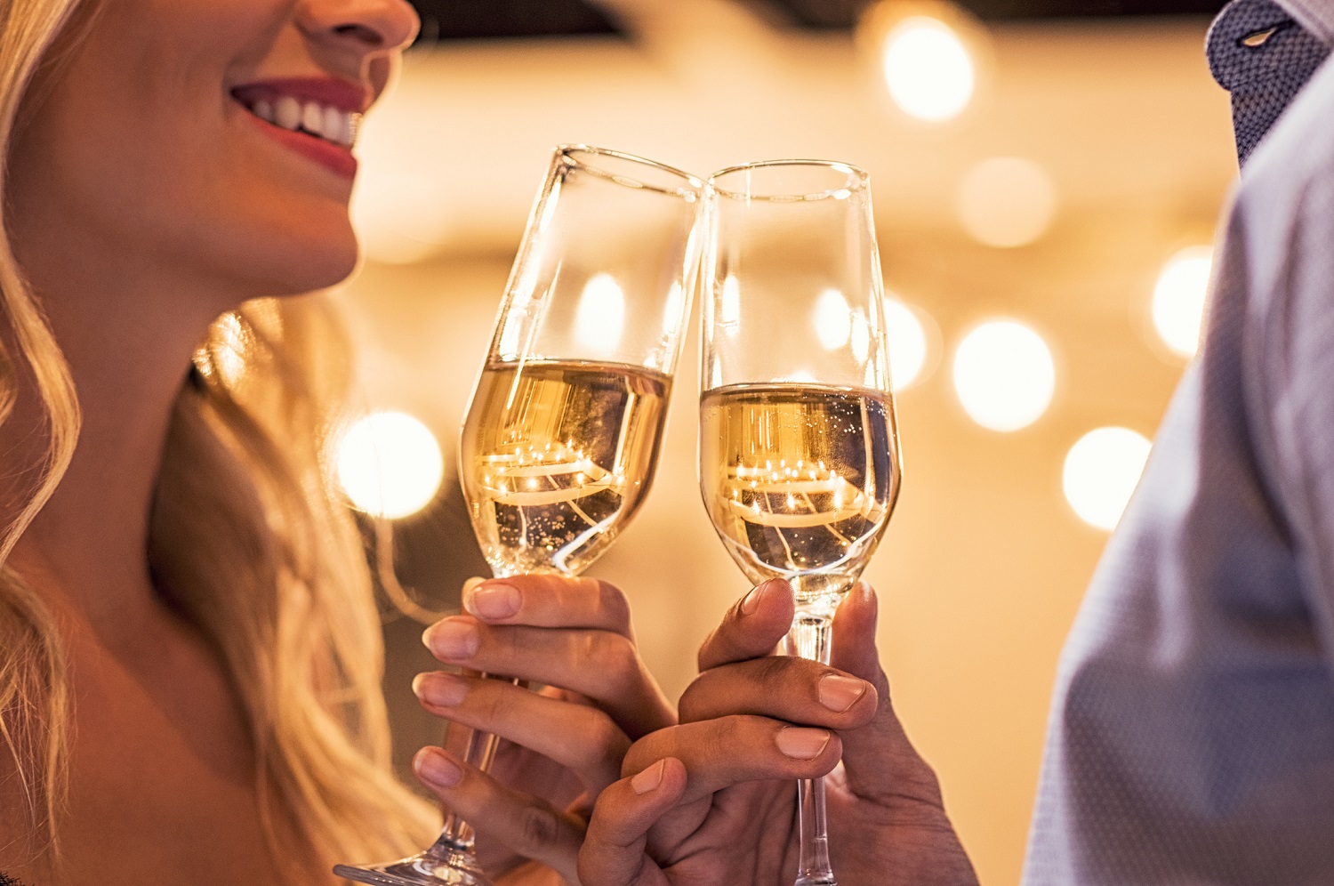 Man and woman toasting champagne flutes under light bulb outdoor. Closeup of boyfriend and girlfriend hands toasting glasses of white wine to celebrate their anniversary. Detail of party celebration.