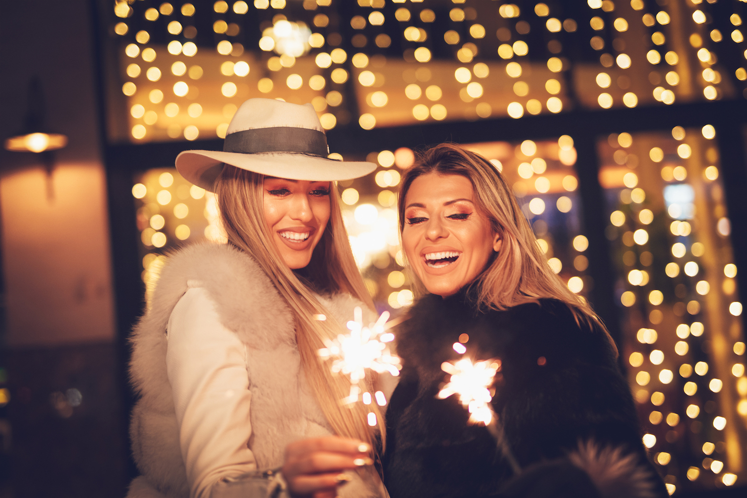 Young beautiful cheerful female friend with sparklers having fun and enjoying in the city street at night at Christmas time. (Young beautiful cheerful couple with sparklers having fun and enjoying in the city street at night 