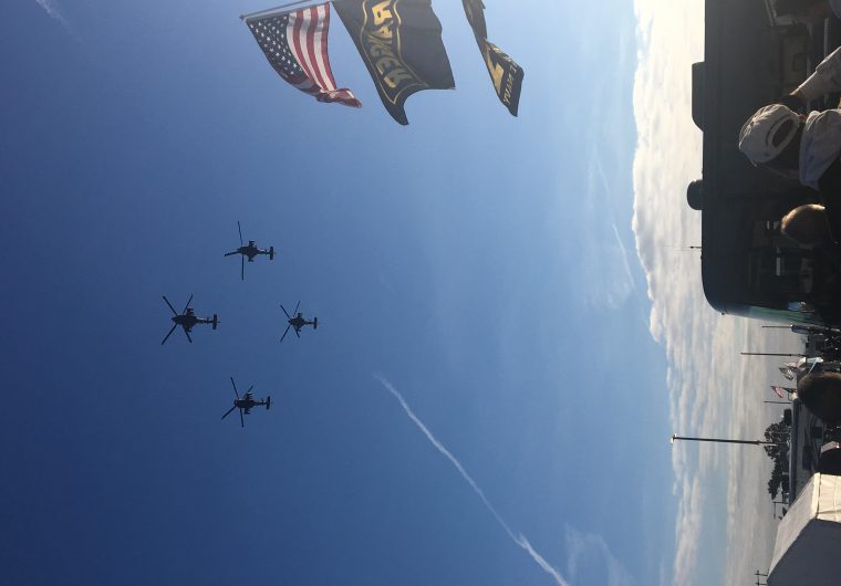 Military jets flying in the blue sky with American flag flowing in the foreground.