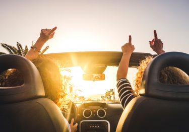 two women having the time of their life with their hands up in a convertible while on a road trip in Florida